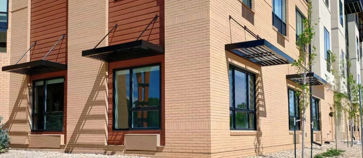 Row of black aluminium louvre awnings with tie-rods over the windows of a brick building